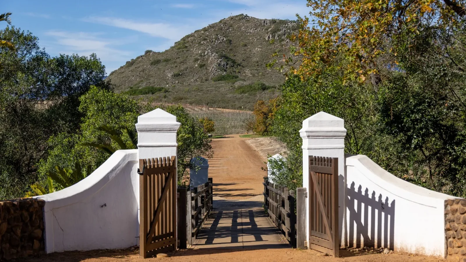 Rustic gated entrance to a scenic trail with lush greenery and a hill under bright blue sky