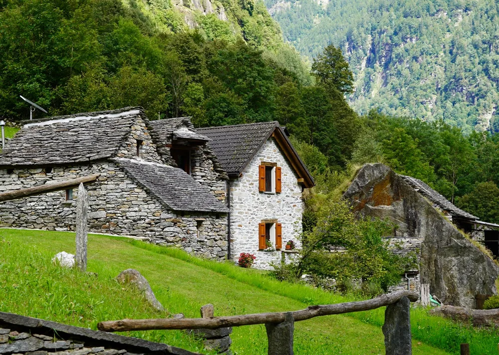 Rustic stone cottage surrounded by lush greenery and mountains