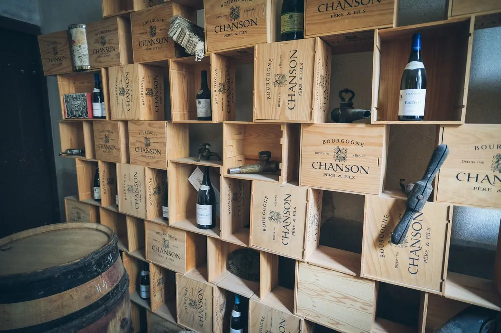 Rustic wine cellar featuring wooden shelves filled with Chanson wine crates and vintage bottles