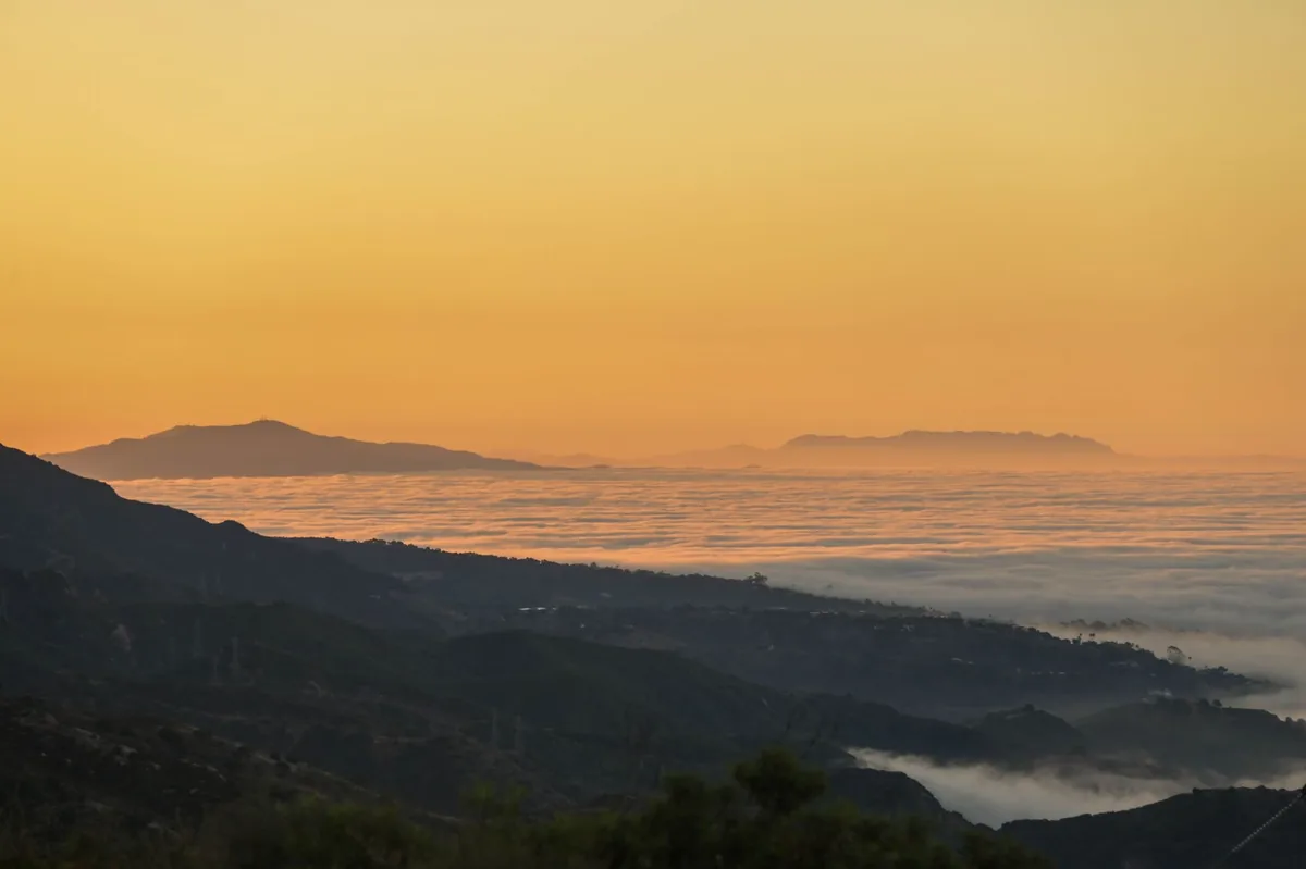 Santa Barbara's landscape during a serene sunrise, with misty clouds and mountain silhouettes