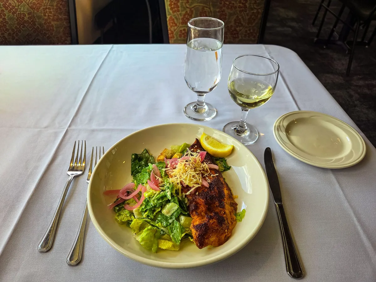 A glass of white wine beside grilled fish and lemon on an outdoor table
