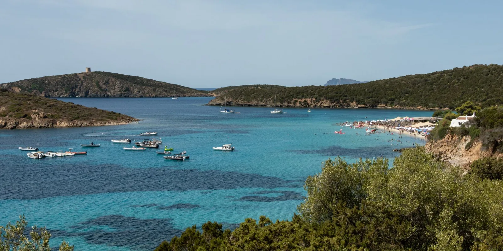 Sardinian coastal view with boats and a sandy beach under a clear blue sky