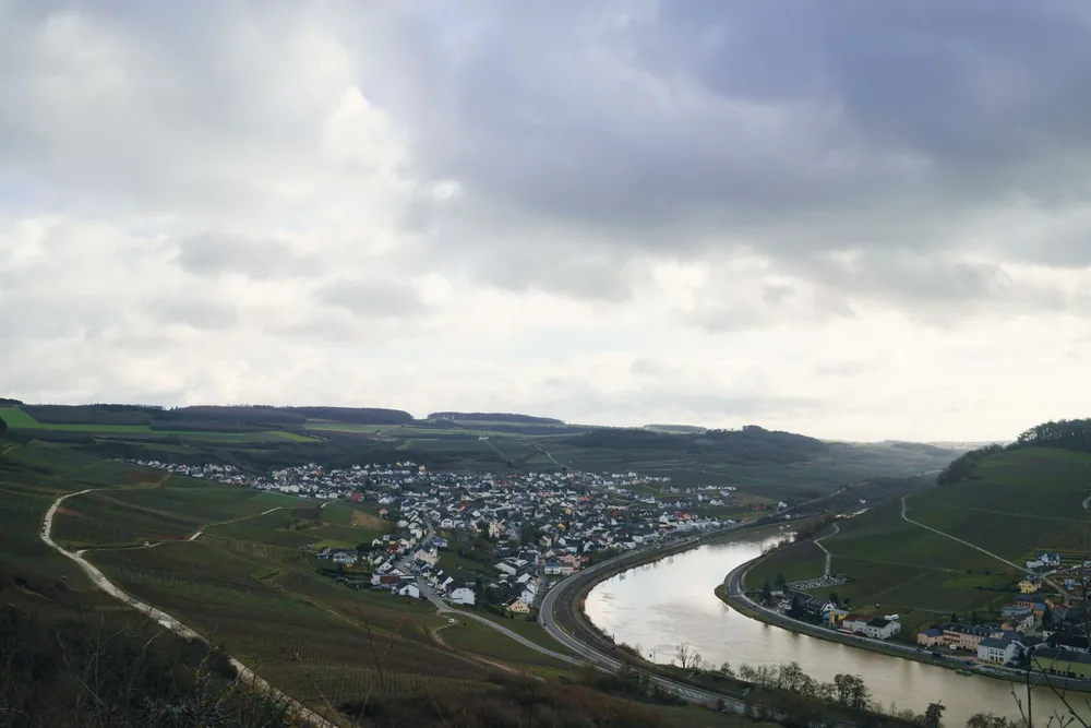 Scenery of green fields and calm river with small settlement under cloudy sky in summer day