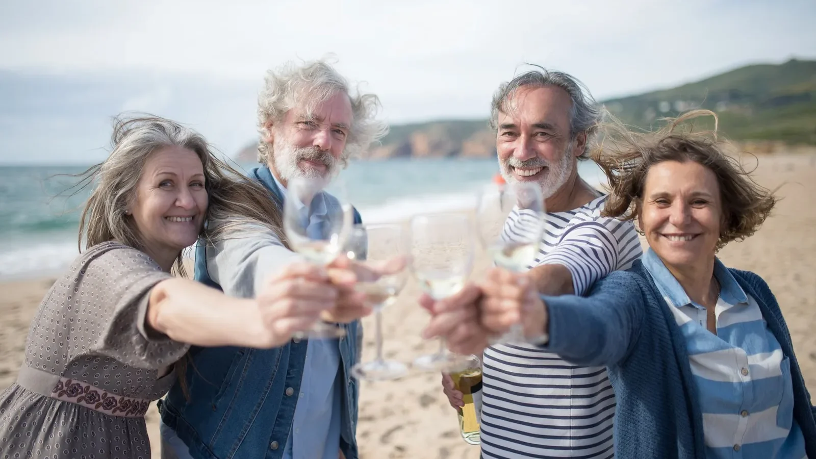 Senior adults enjoying a coastal toast with wine on a Portuguese beach, celebrating friendship