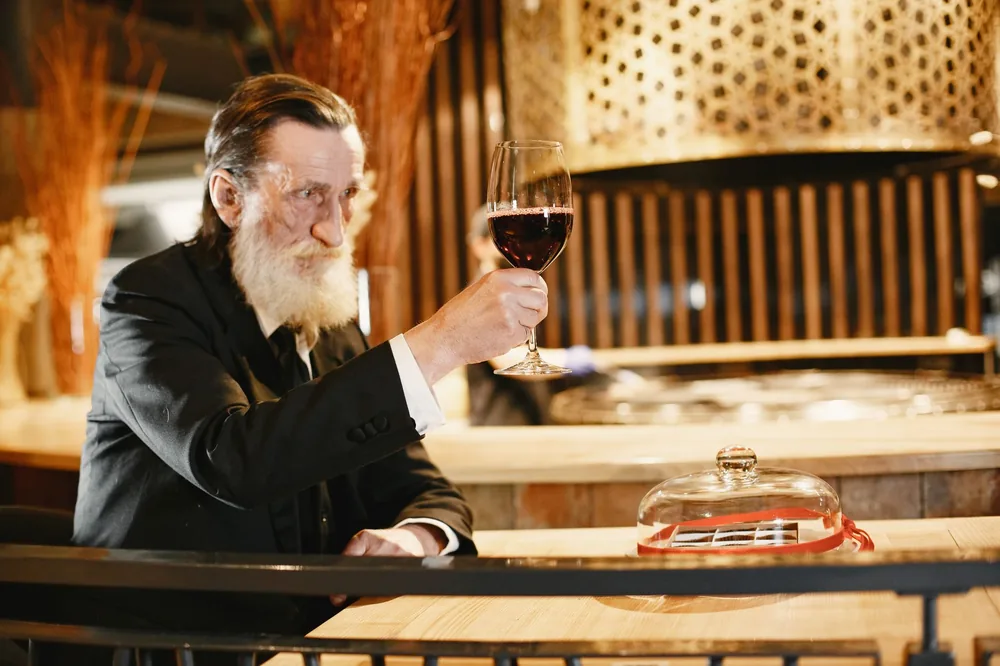 Senior man in a black suit raising a wine glass in an elegant restaurant setting