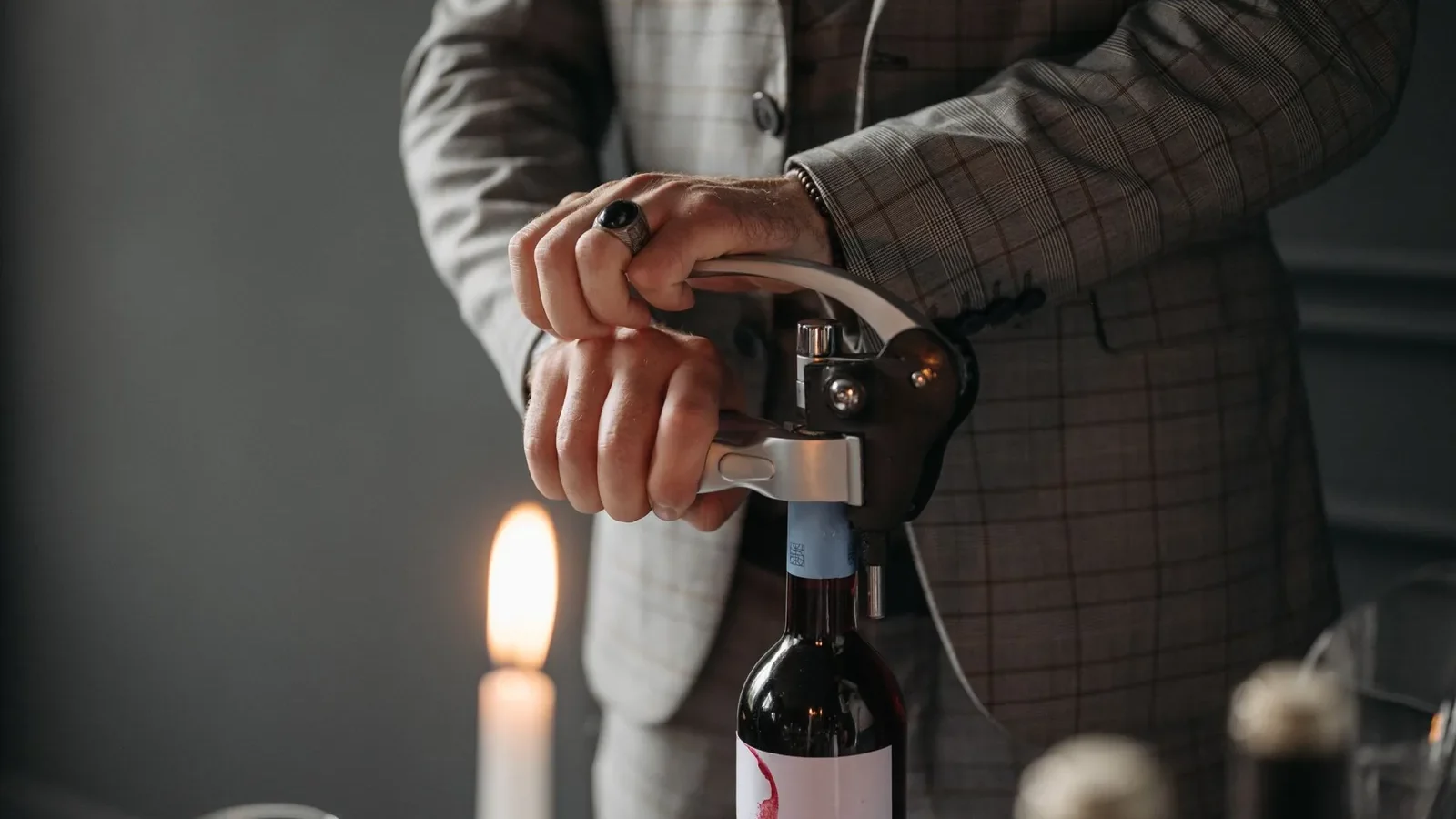 Setting of a person opening a wine bottle with a corkscrew next to candlelight