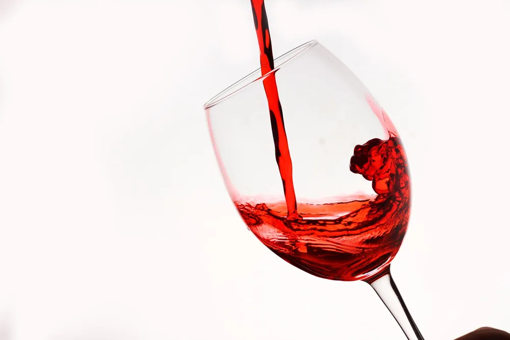 Shot of red wine being poured into a tilting glass against a white background