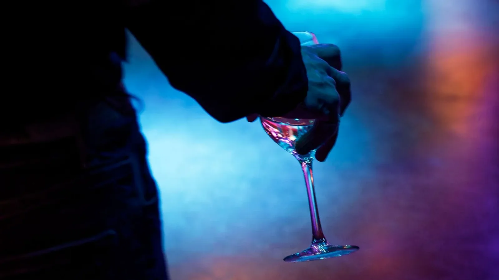 Silhouette of a person holding a wine glass against a nightclub background