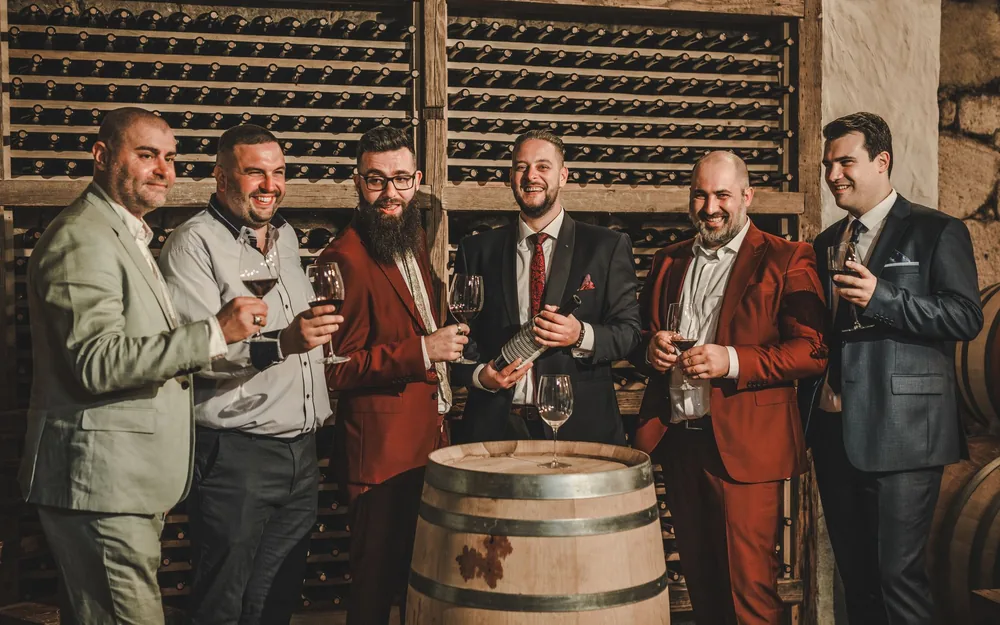 Six men in suits enjoying red wine in an upscale wine cellar setting