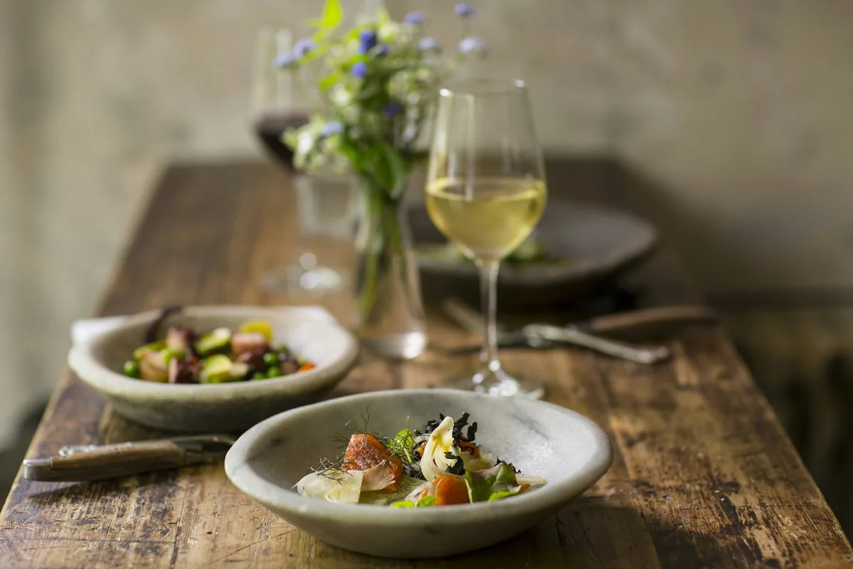 A glass of pale white wine beside a plate of roasted fish and greens