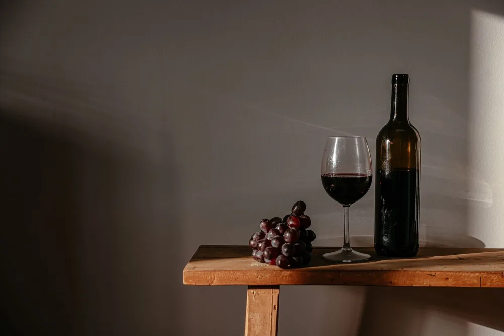 Sophisticated still life featuring red wine, a bottle, and grapes on a rustic wooden surface