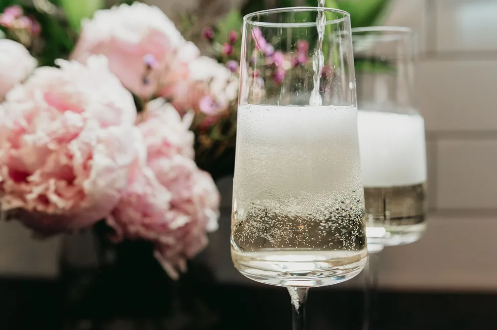 Sparkling champagne being poured into a glass with peonies in the background
