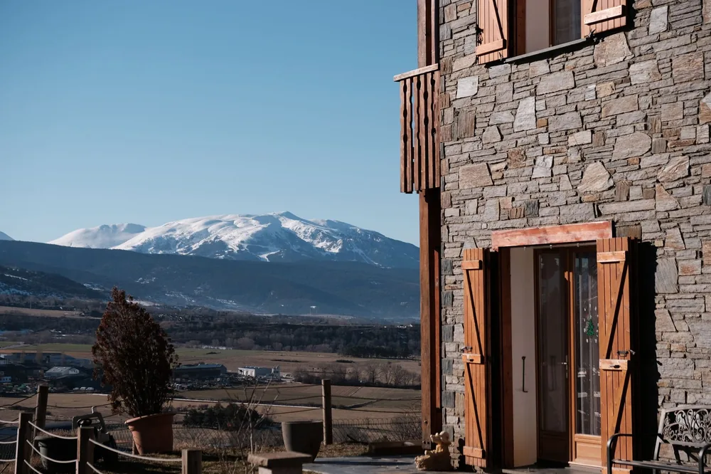 Stone house with wooden shutters overlooking snow-capped mountains in a clear winter day