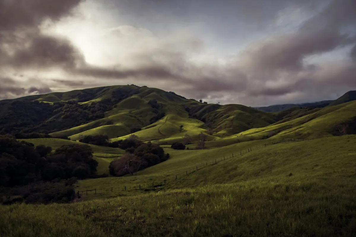 Rural landscape of Cambria, CA with rolling green hills under dramatic clouds
