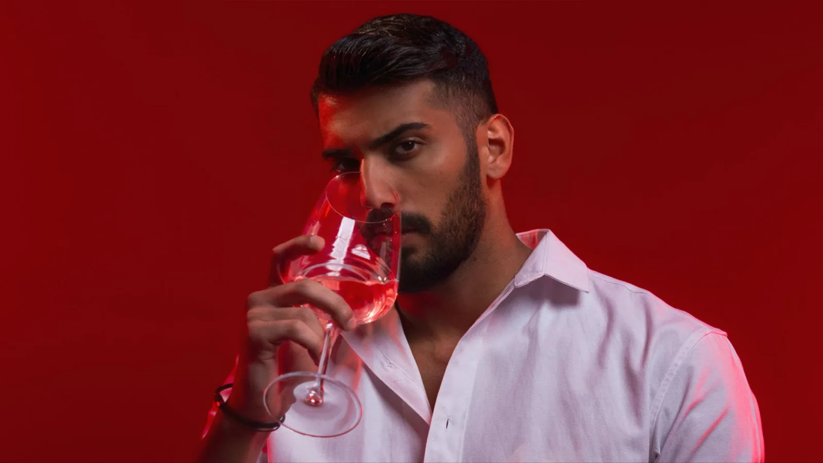 Stylish man in white shirt holding a wine glass against a red background