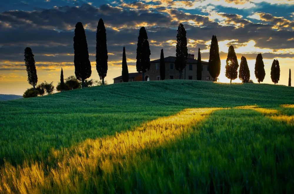 Sunrise over a scenic Tuscan landscape with cypress trees and farmhouse