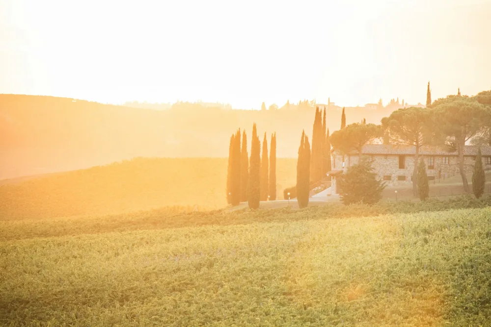 Sunrise over tuscan hills, cypress trees, and a building