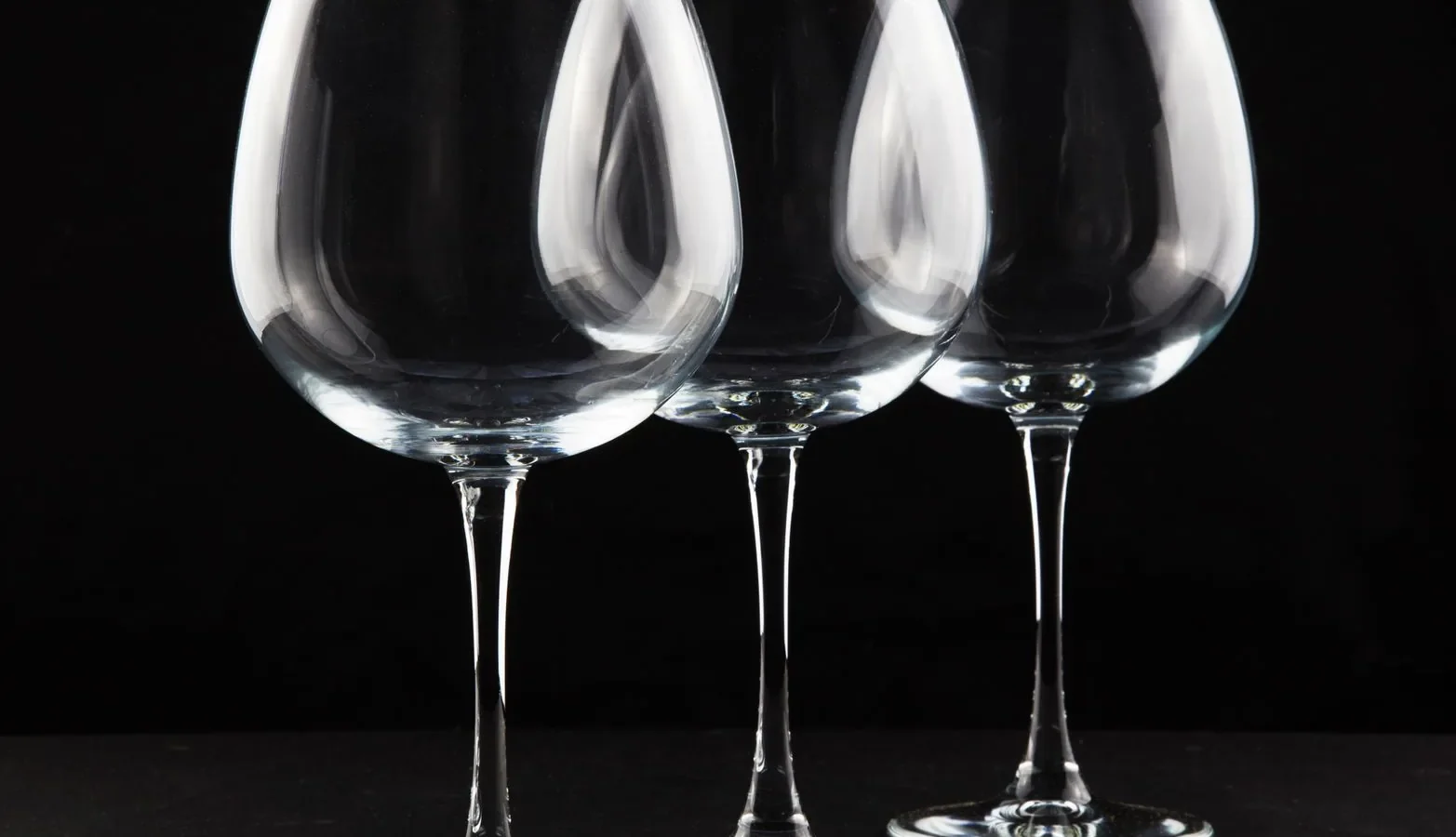 Three crystal wine glasses elegantly arranged against a black backdrop, perfect for dining and lifestyle themes