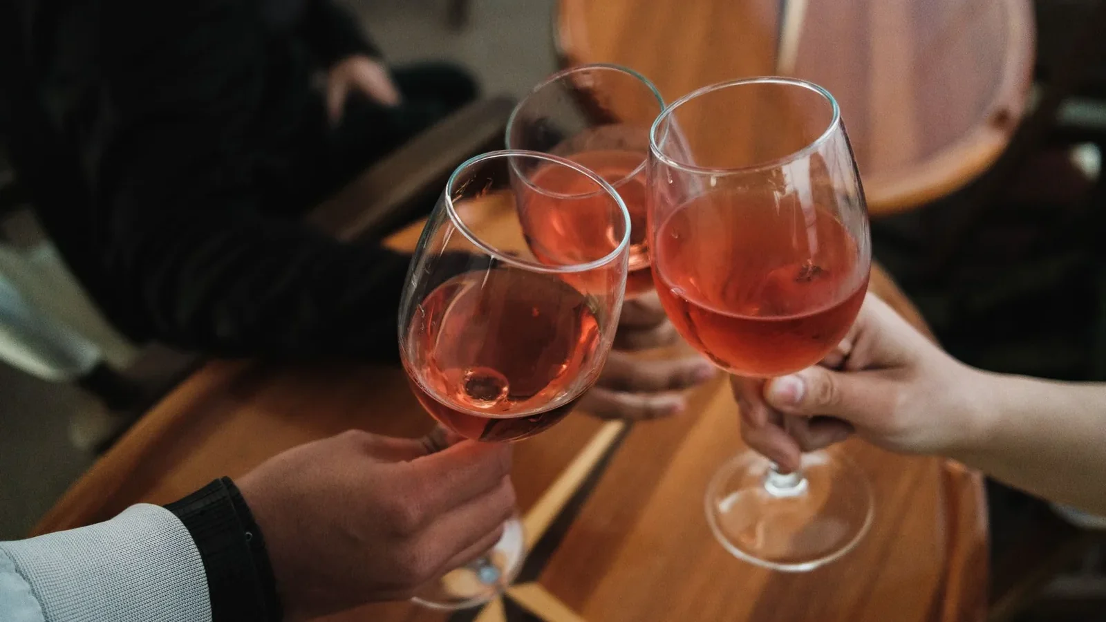 Three friends toasting with rosé wine glasses over a wooden table indoors
