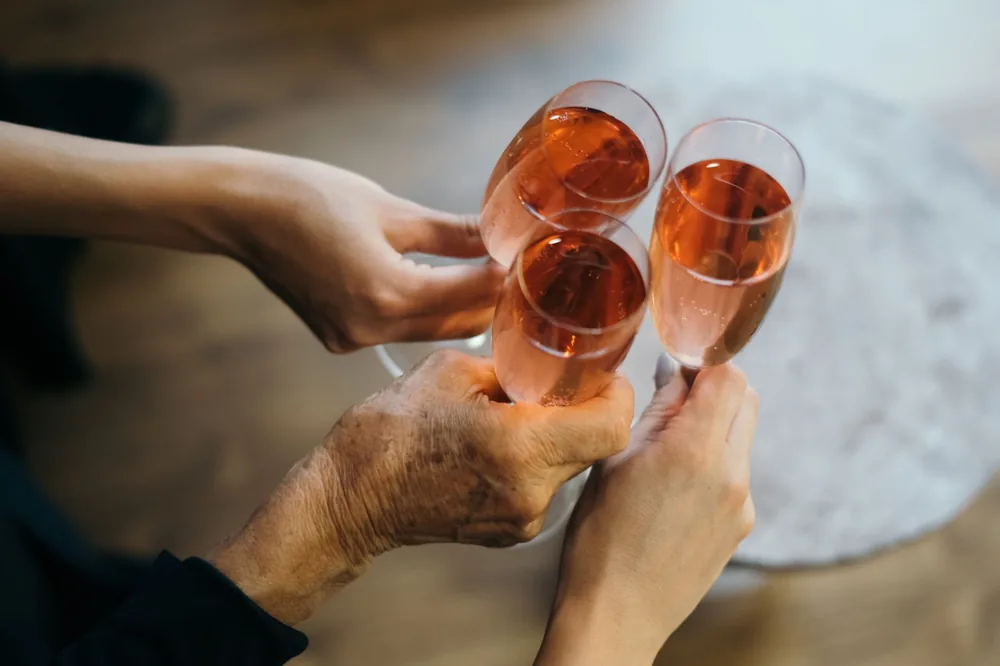 Three hands holding and clinking rose champagne glasses in a celebratory toast