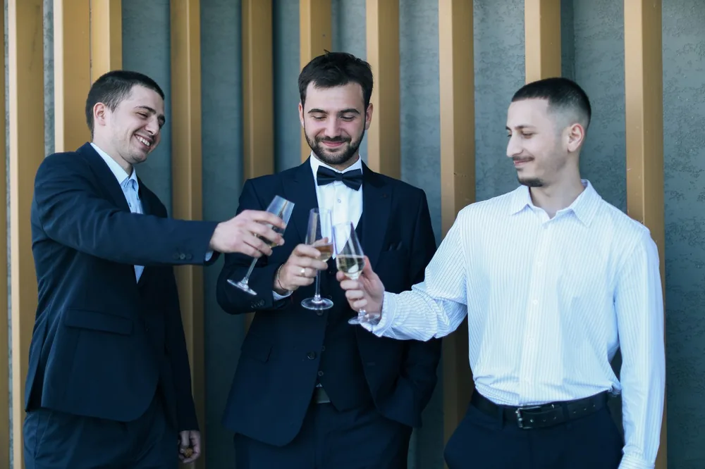 Three men in formal wear toasting with champagne glasses, celebrating outdoors