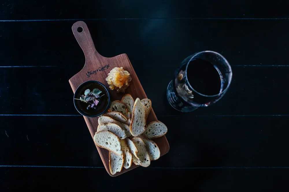 Top view of a cutting board with bread slices, herbs, and wine, creating a rustic snack setup
