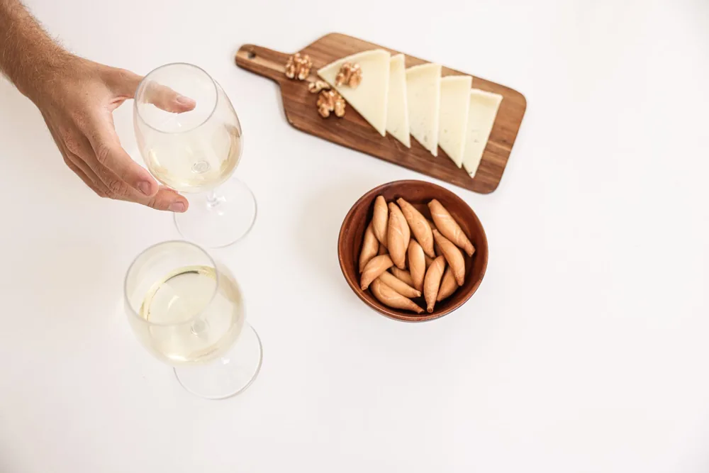 Top view of cheese slices, breadsticks, and wine glasses on a white surface for an elegant dining setup