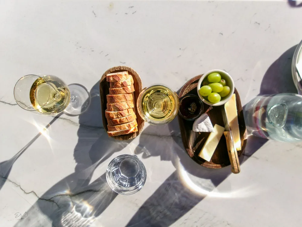 Top view of wine, cheese, and bread on a marble table with sunlight reflections, perfect for a stylish gathering