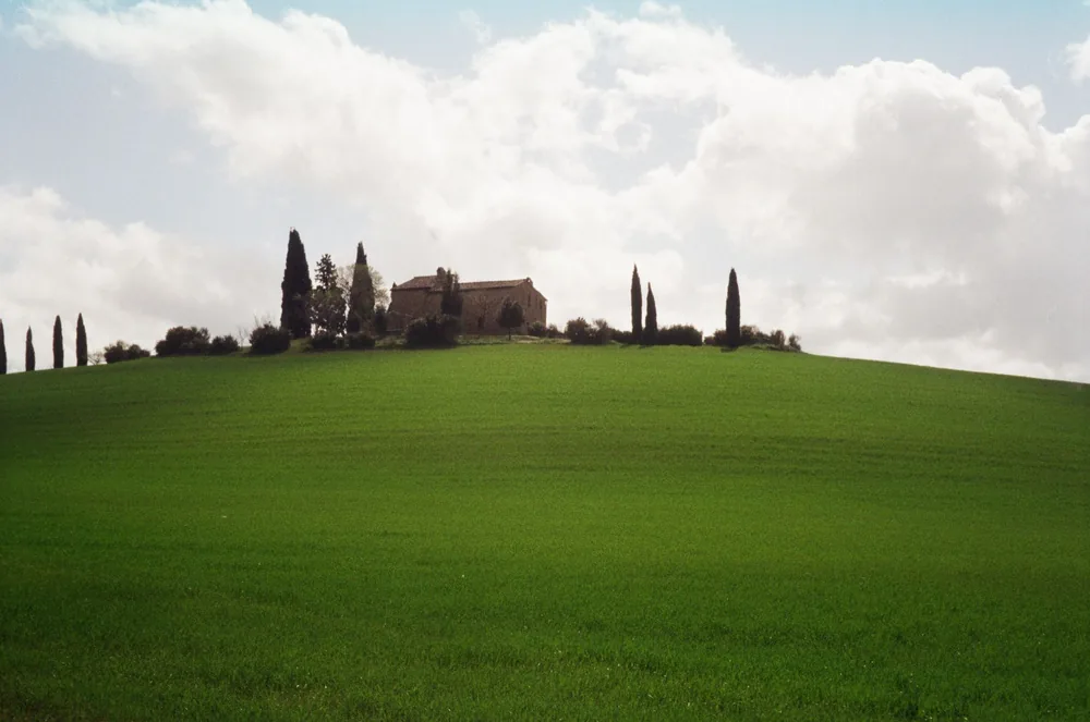 Tuscan landscape with a farmhouse atop a lush green hill dotted with cypress trees