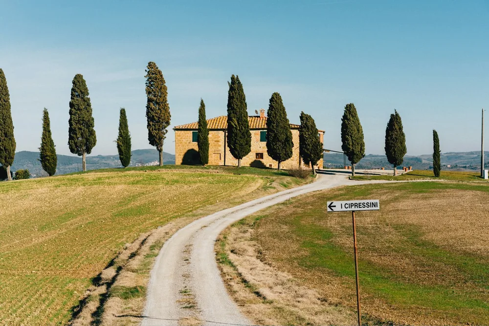 Tuscan landscape with a winding road, farmhouse, and cypress trees