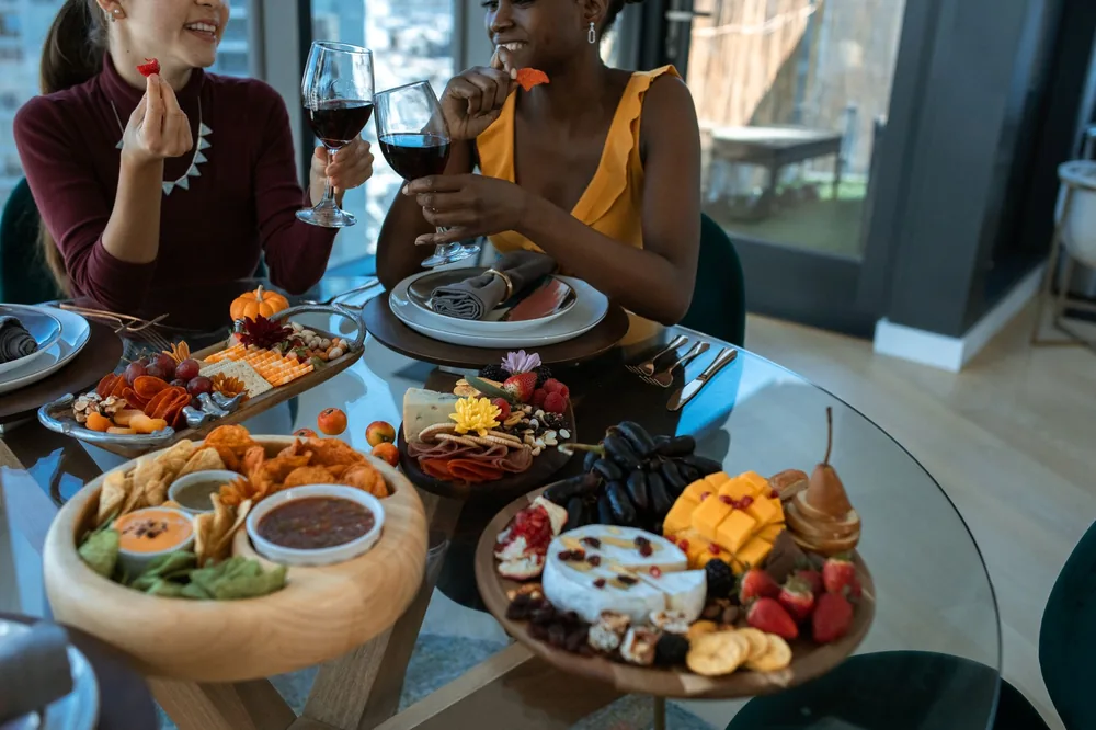 Two adults enjoy wine and a colorful charcuterie board indoors, embodying warmth and friendship