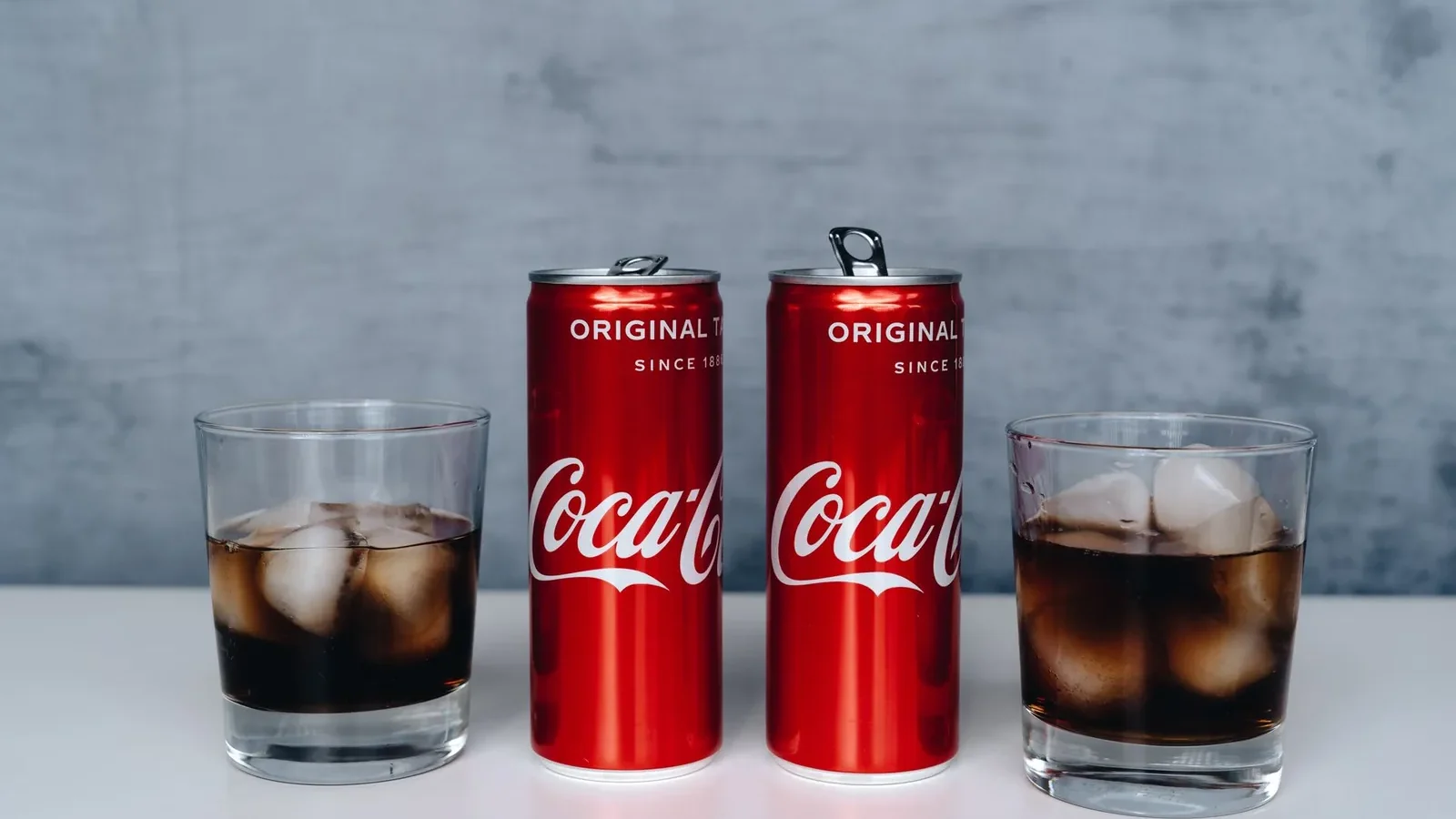 Two cans of soda with ice-filled glasses on a minimalistic background