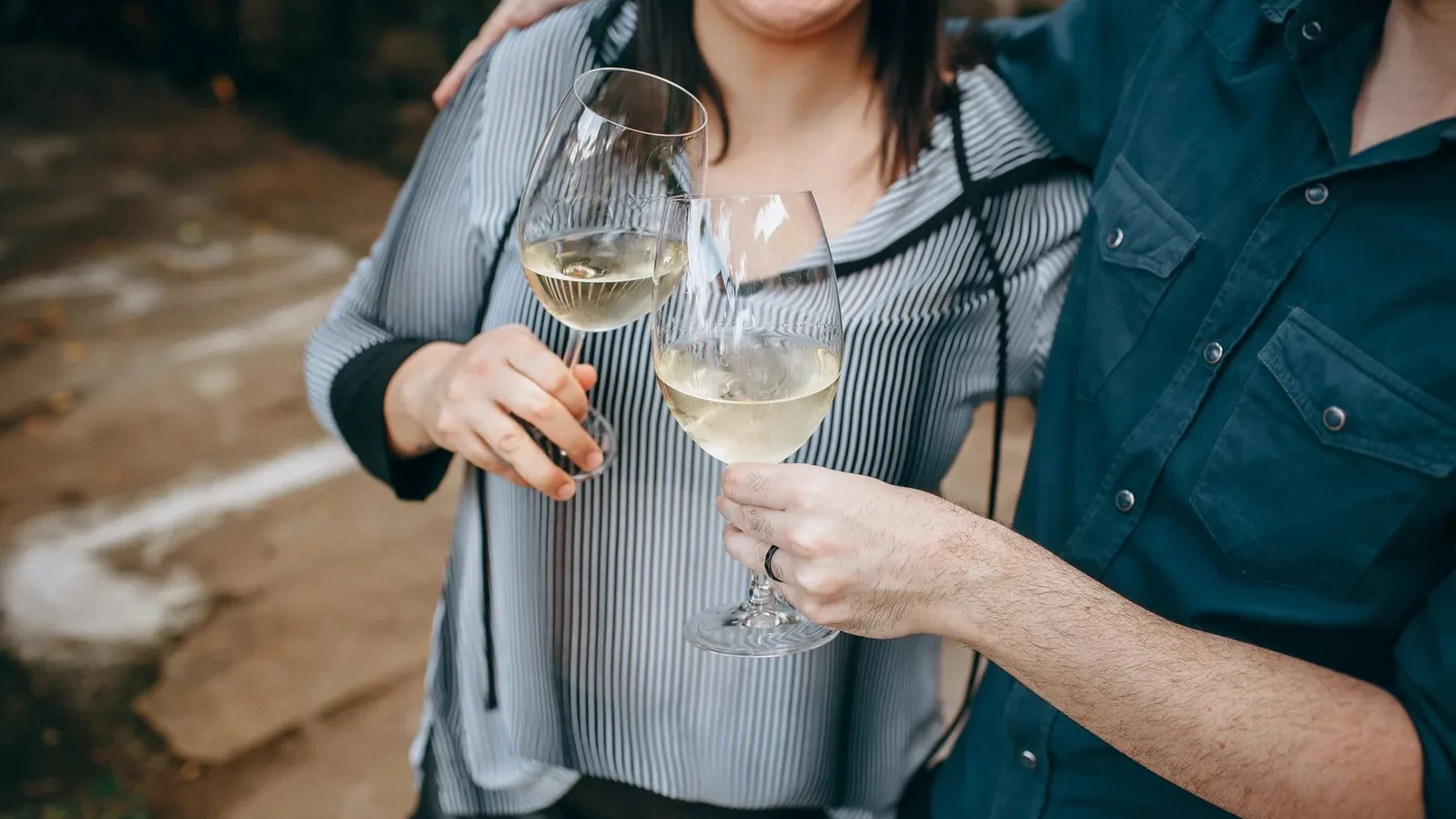 Two friends toasting with glasses of white wine in an outdoor setting, celebrating a joyful occasion