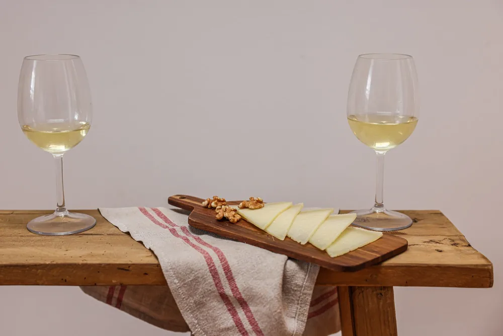 Two glasses of white wine with cheese and walnuts on a wooden board for a cozy gathering