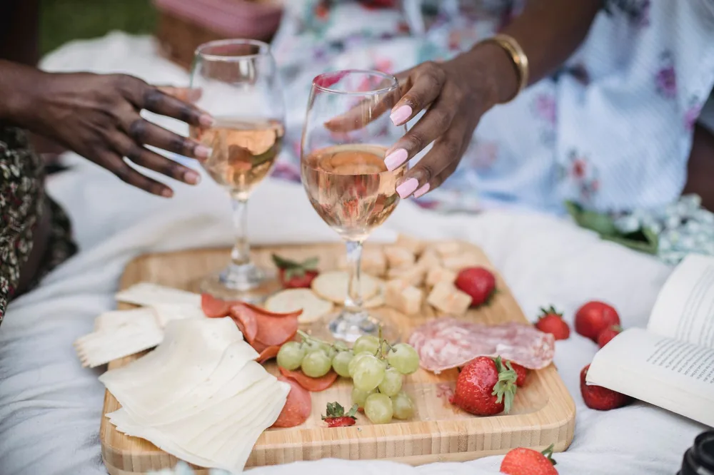 Two people enjoying a summer picnic with wine and cheese outdoors