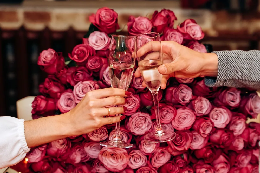 Two people toasting with champagne glasses in front of roses