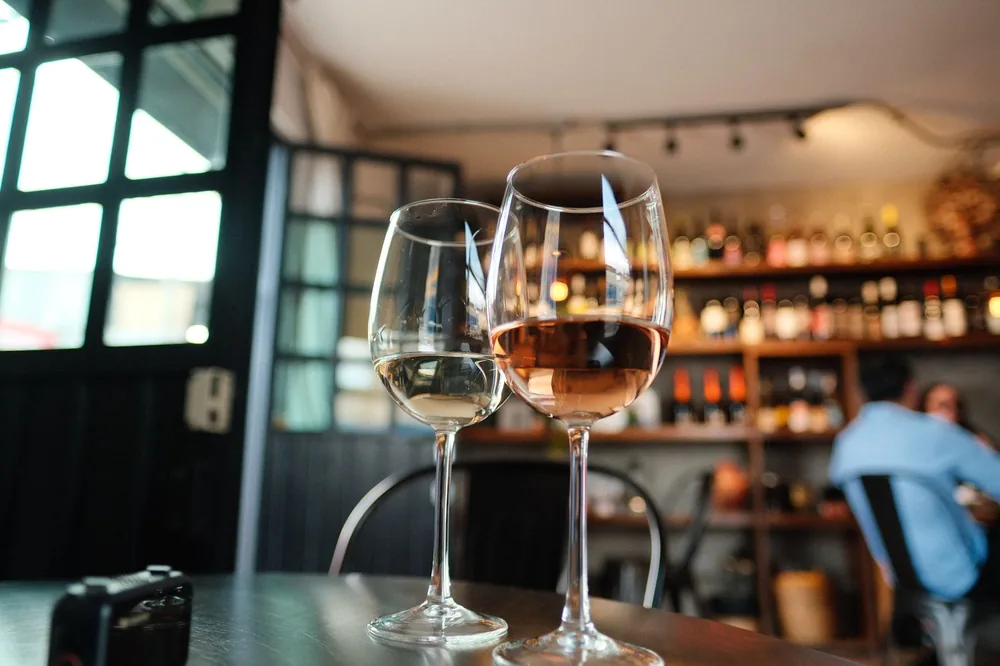 Two wine glasses on a table in a cozy bar with bottles in the background, perfect for social or lifestyle themes
