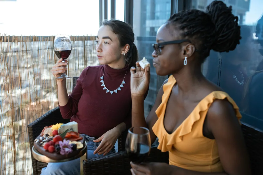 Two women savoring cheese and wine on a balcony, capturing a moment of leisure and friendship