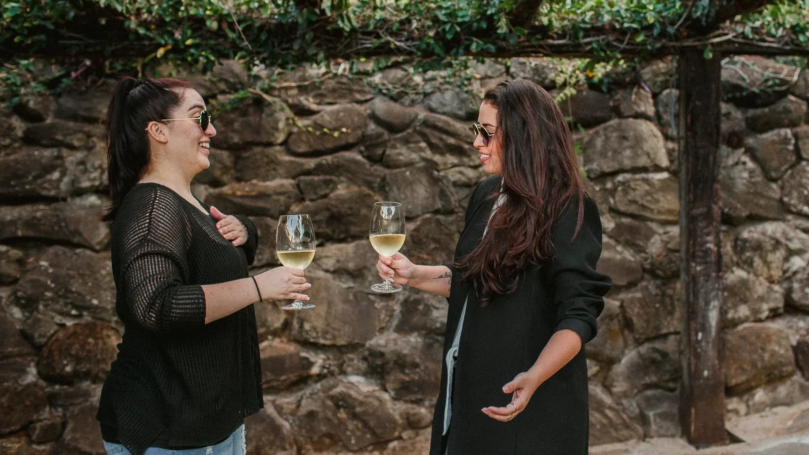 Two women share a joyful moment with wine glasses outdoors, capturing relaxing fall vibes