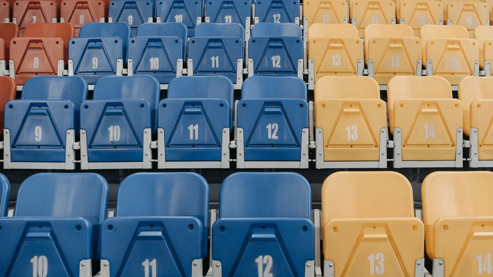 Uniform rows of red, blue, and yellow stadium seats with numbers visible