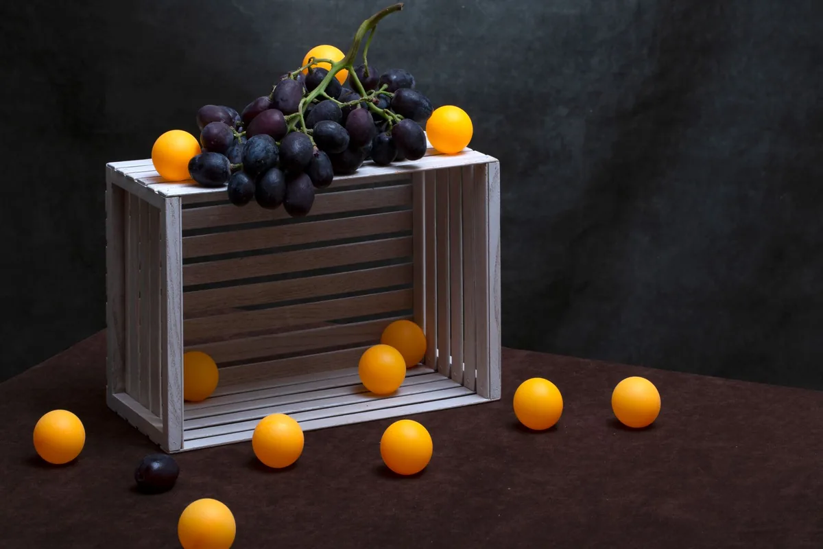 A creative still life with grapes and yellow ping pong balls on a wooden crate