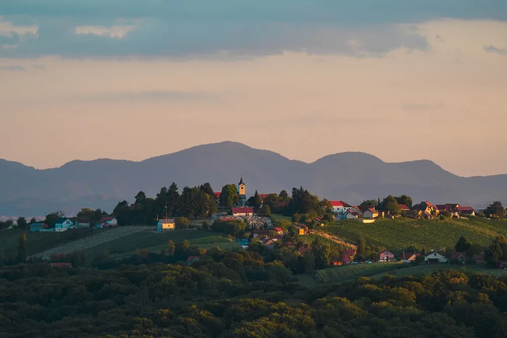 Village landscape at sunset with a church, vineyards, and mountains in the background