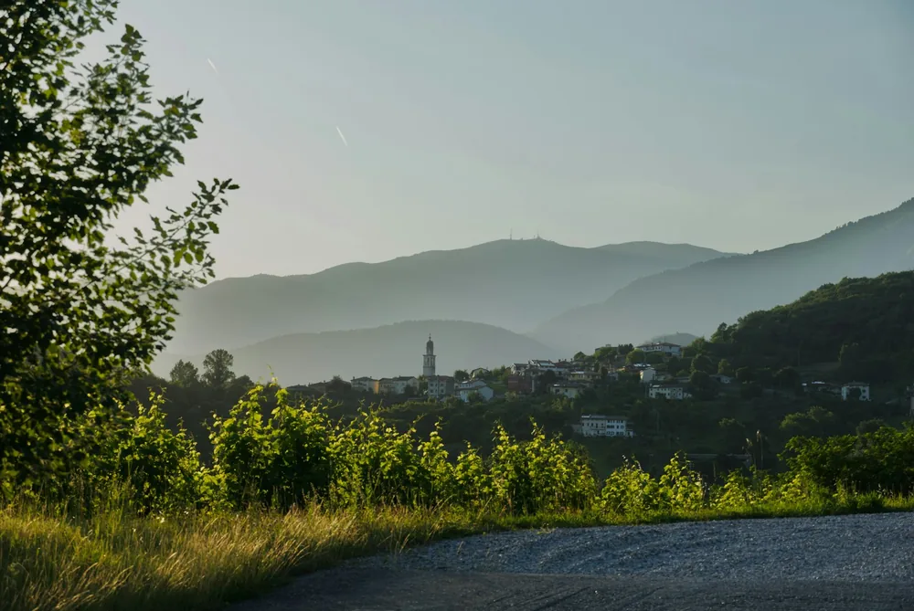 Village with church tower, green foliage, and hazy mountains