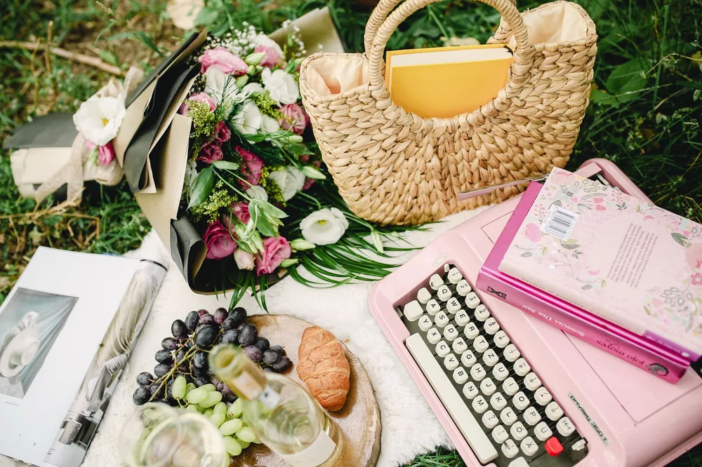 Vintage pink typewriter and picnic essentials on grass for a serene outdoor setting