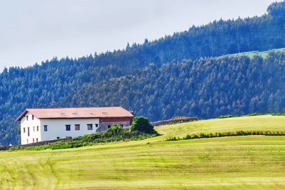 White house nestled in lush greenery and hills, set against a forested backdrop