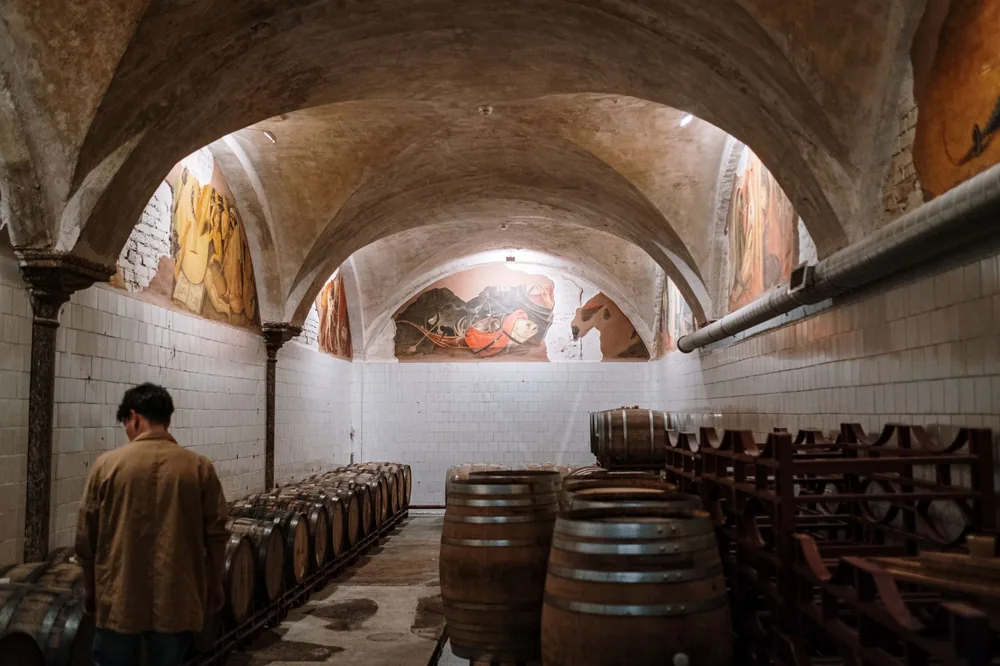 Winery cellar with aged barrels under arched ceilings, adorned with art