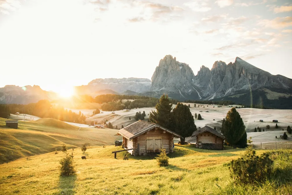 Wooden cabins in an alpine meadow with mountains at sunset